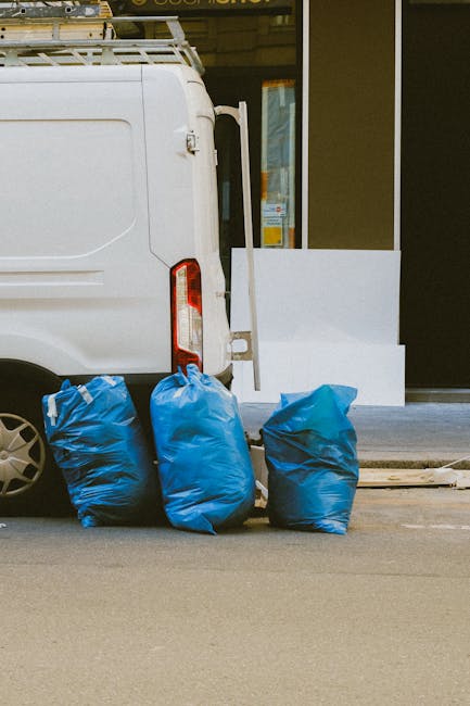 A collection of overflowing waste bins and scattered rubbish on a paved urban pavement, including large black, red, and black bins filled with discarded paper, cardboard, plastic, and miscellaneous wa